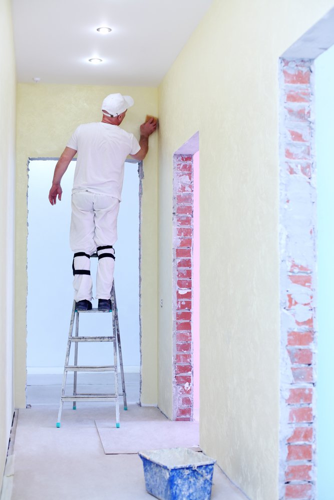 Een persoon reinigt een spachtelputz muur met een spons en ontvettingsmiddel, waardoor de muur weer fris en schoon wordt.