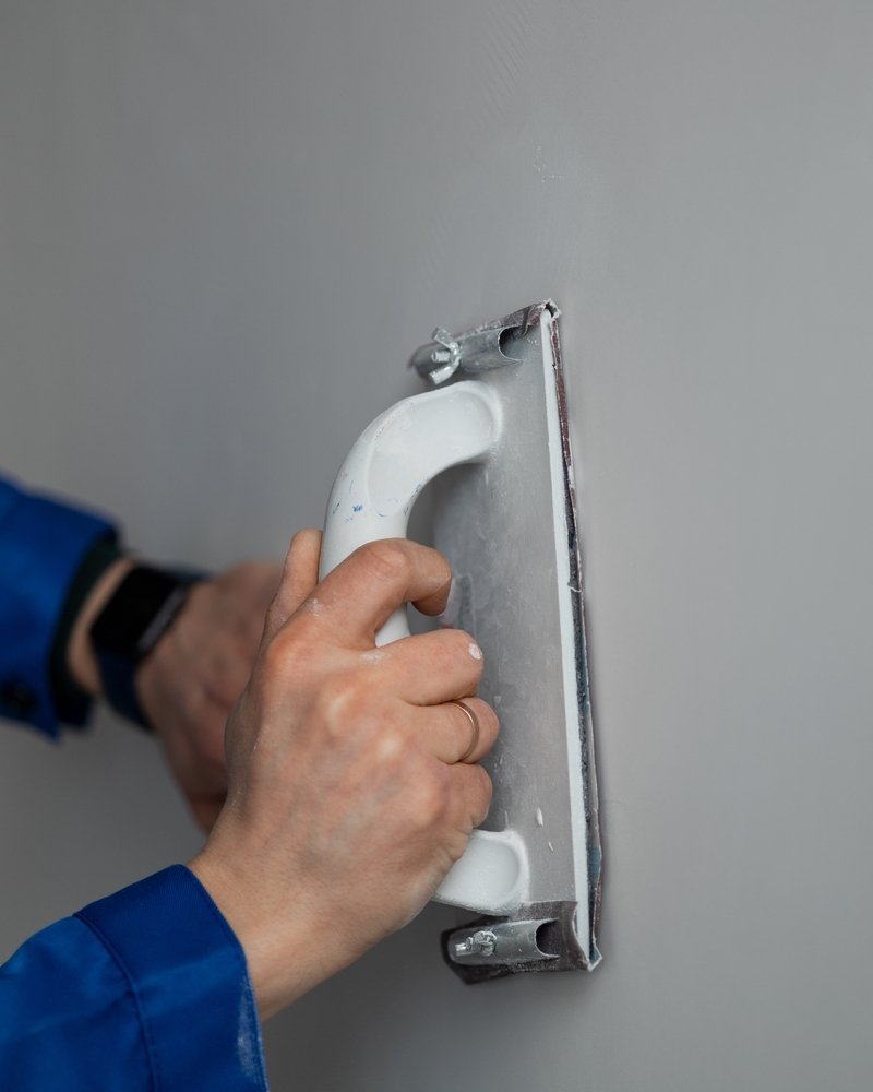 Een persoon brengt spachtelputz aan op een muur met een spaan, nauwkeurig werkend om een gelijkmatige afwerking te bereiken.