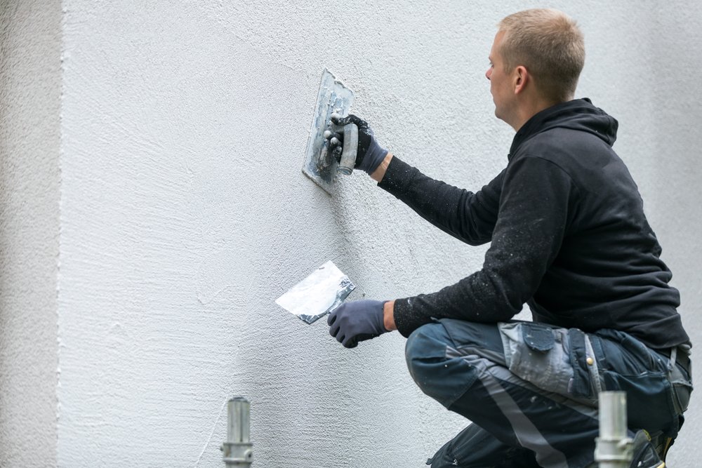 Een persoon gebruikt een afbikbeitel om spachtelputz van de muur te verwijderen, een stap in het renovatieproces van de wandafwerking.