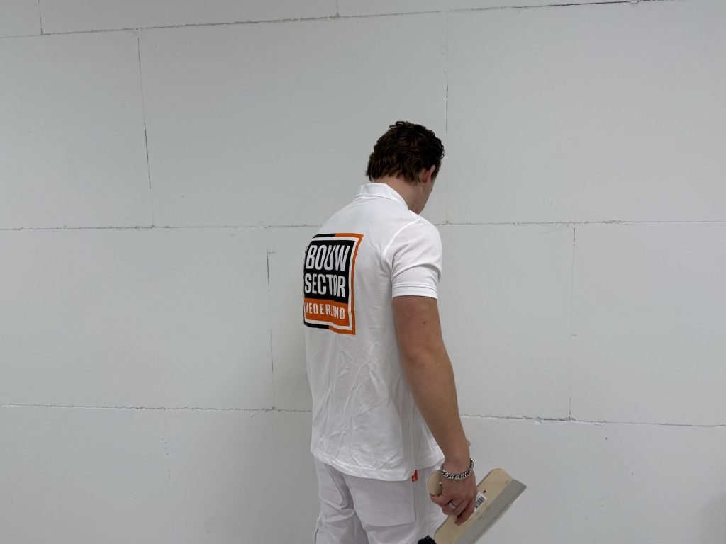 Stukadoor van Bouwsector Nederland bekijkt een kale wand met zichtbare voegen, met een spaan in de hand