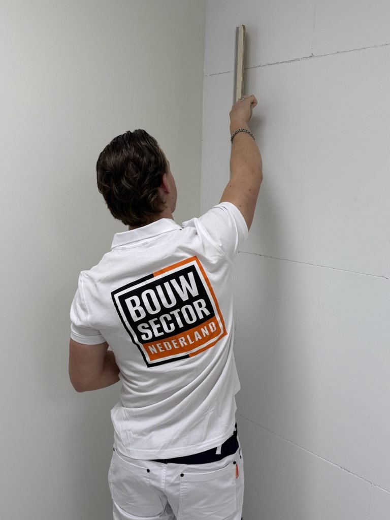 Stukadoor van Bouwsector Nederland reikt met een lange spaan naar de bovenkant van een wand